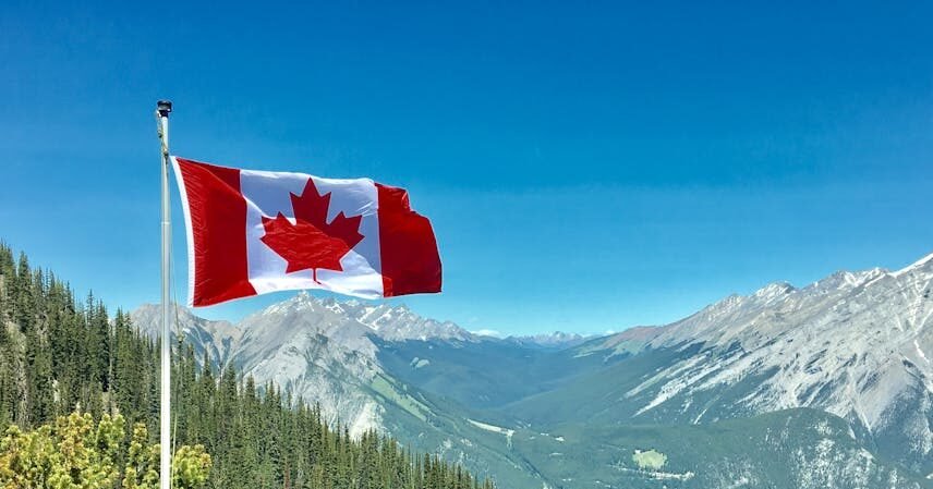 Canadian flag waving atop a scenic mountain view with blue skies and lush greenery.